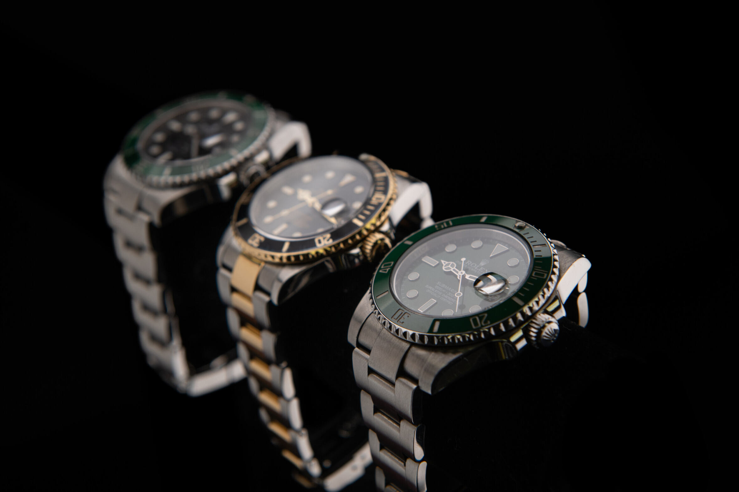 3 aligned Rolex Submariner watches are shown with a black background.